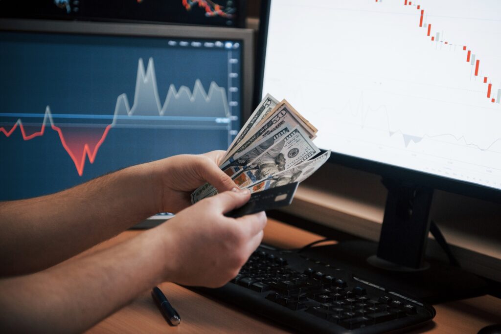 human hands holds money in the office with multiple screens with graphs
